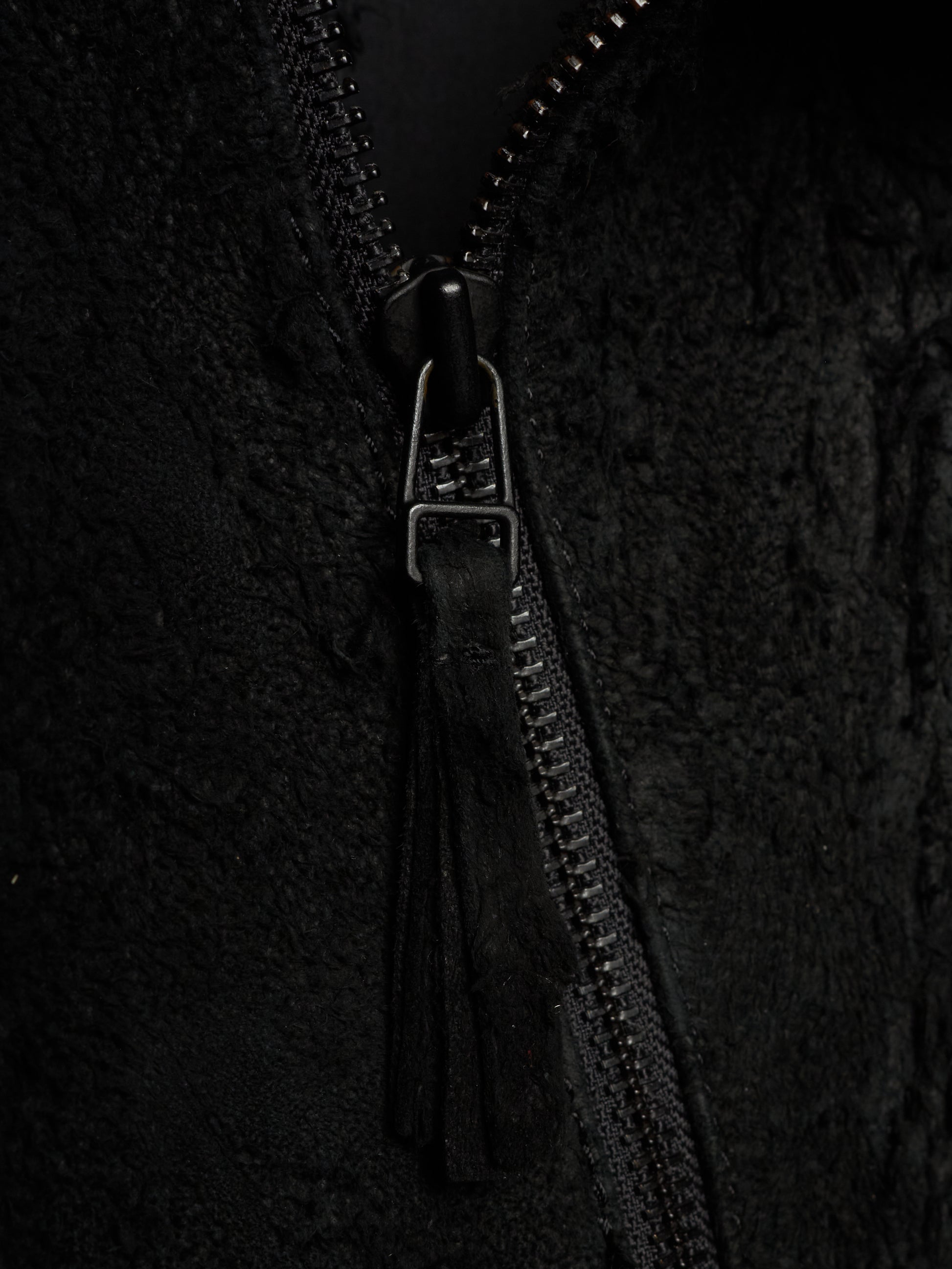 Close-up of a black textured zippered jacket with a black tassel zipper pull and a silver-toned metal slider.