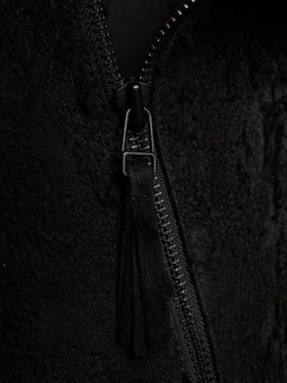 Close-up of a black textured zippered jacket with a black tassel zipper pull and a silver-toned metal slider.
