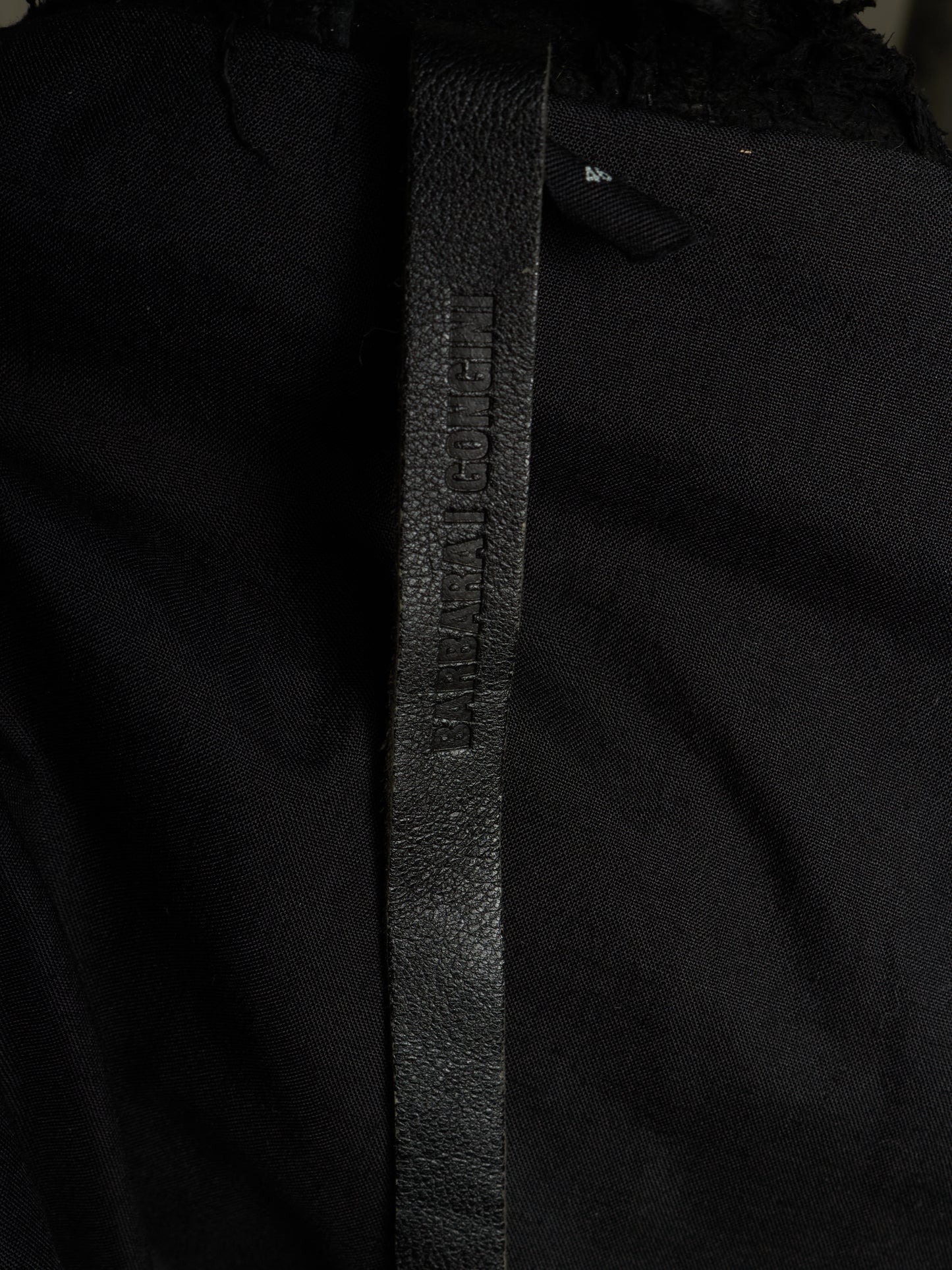 Close-up of a black textured leather belt with 'BURGA' debossed vertically, attached to a black garment.