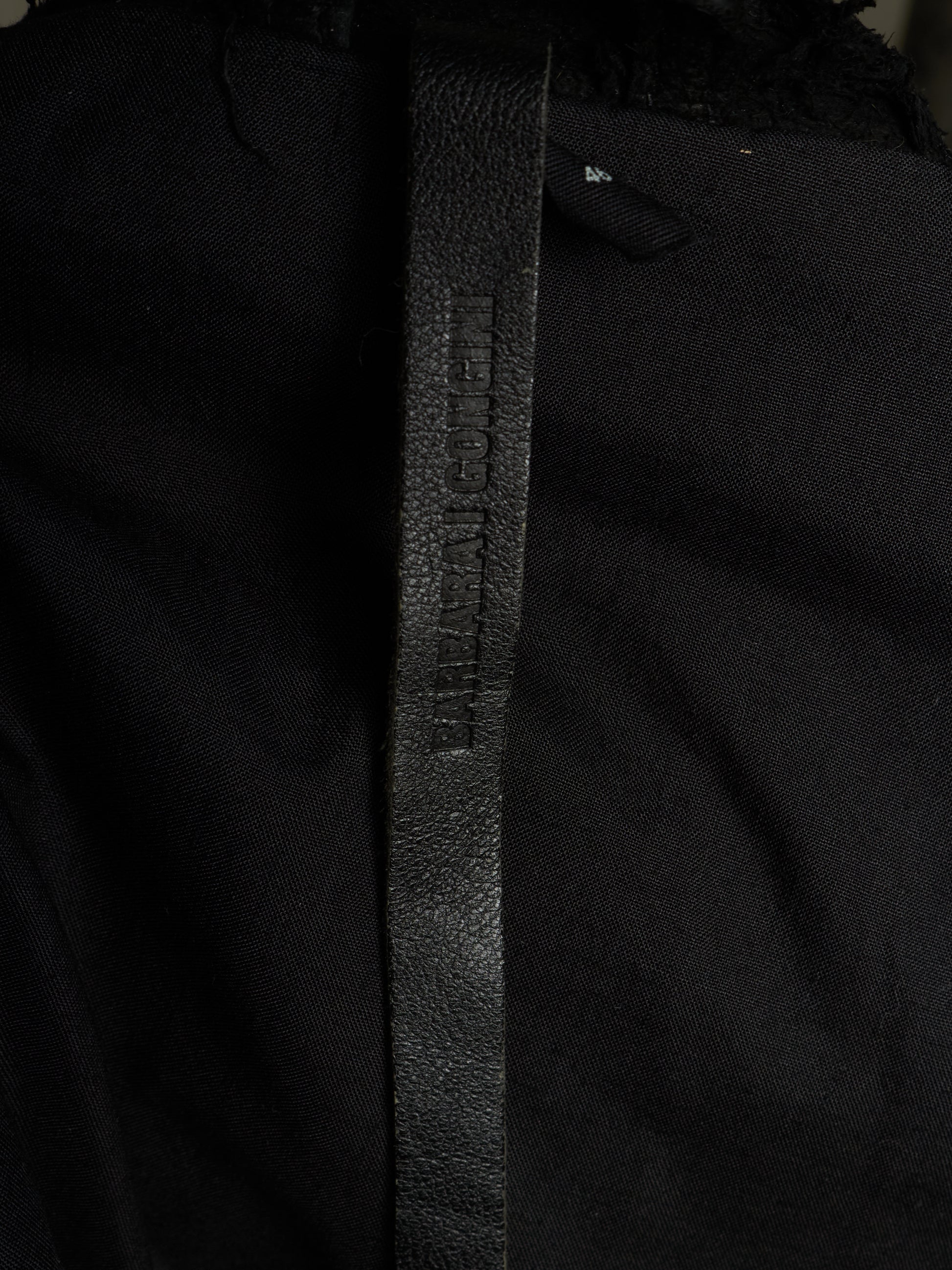 Close-up of a black textured leather belt with 'BURGA' debossed vertically, attached to a black garment.