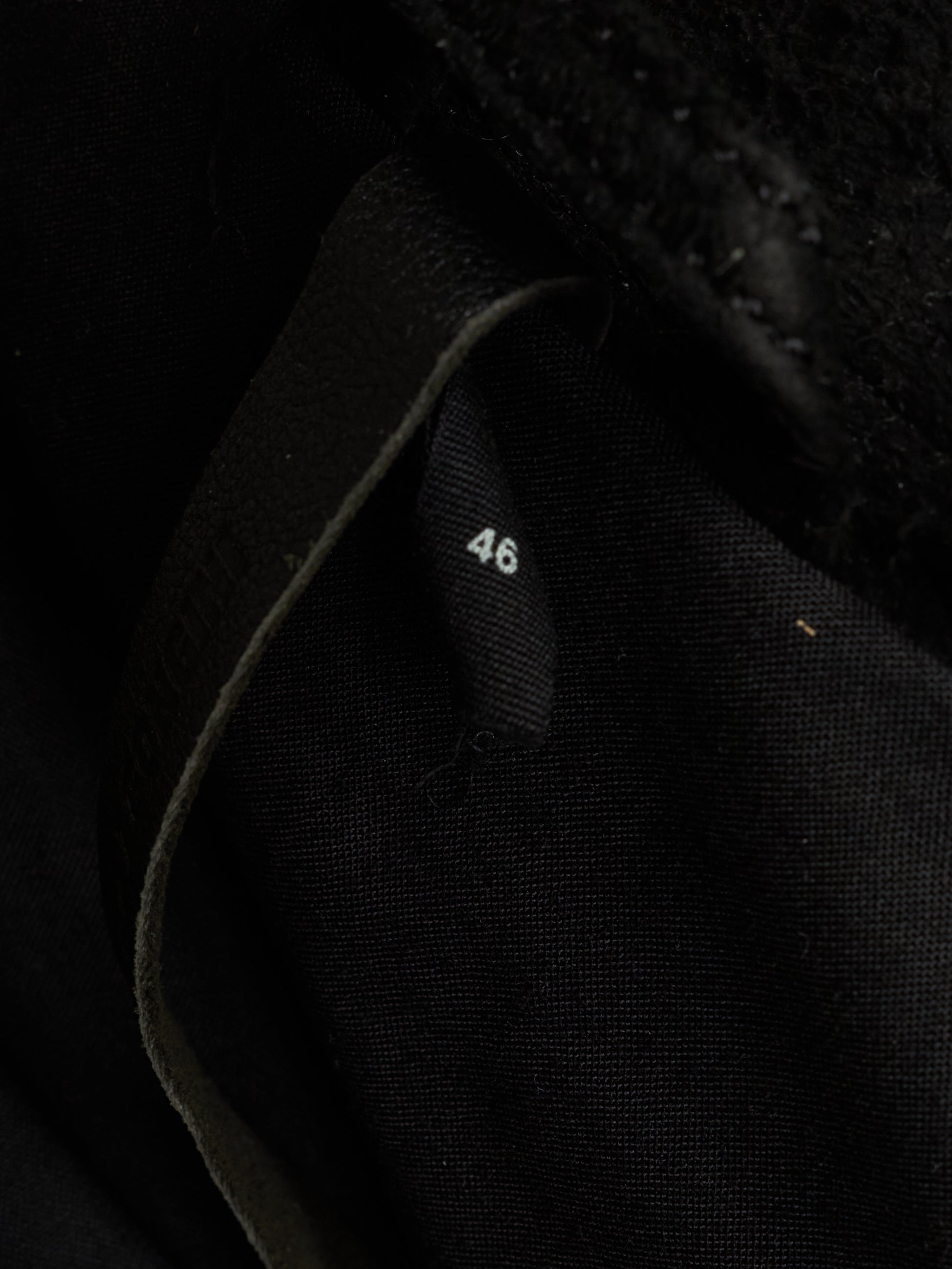 Close-up of a black textured fabric item with a small white size marking reading '46' on a dark interior tab.