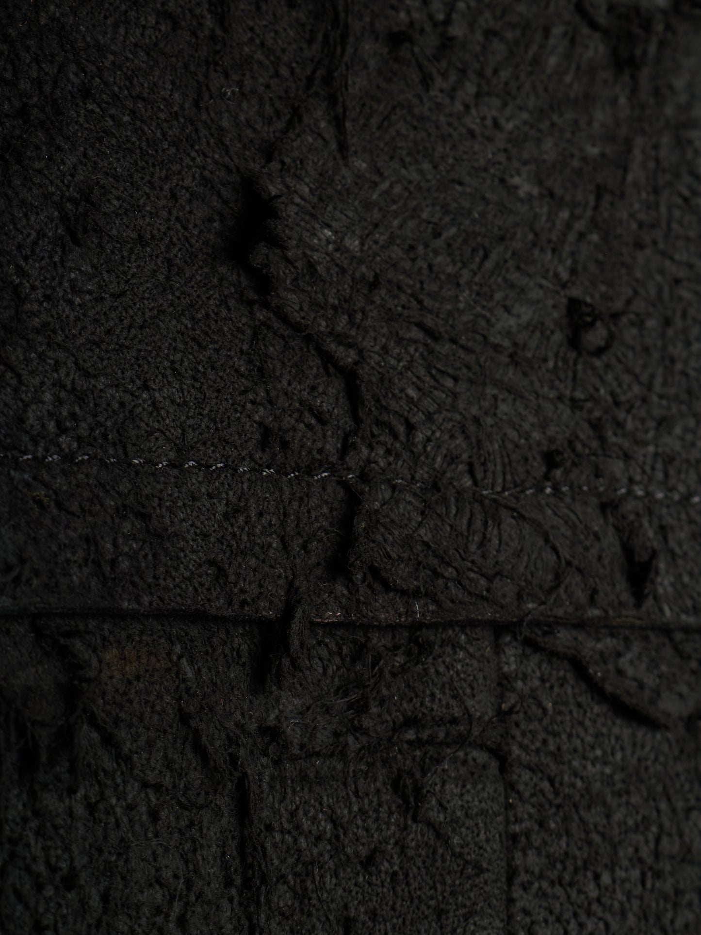 A close-up of a dark textured material with a heavily distressed, cracked, and weathered appearance, showing fine grain and deep shadows.