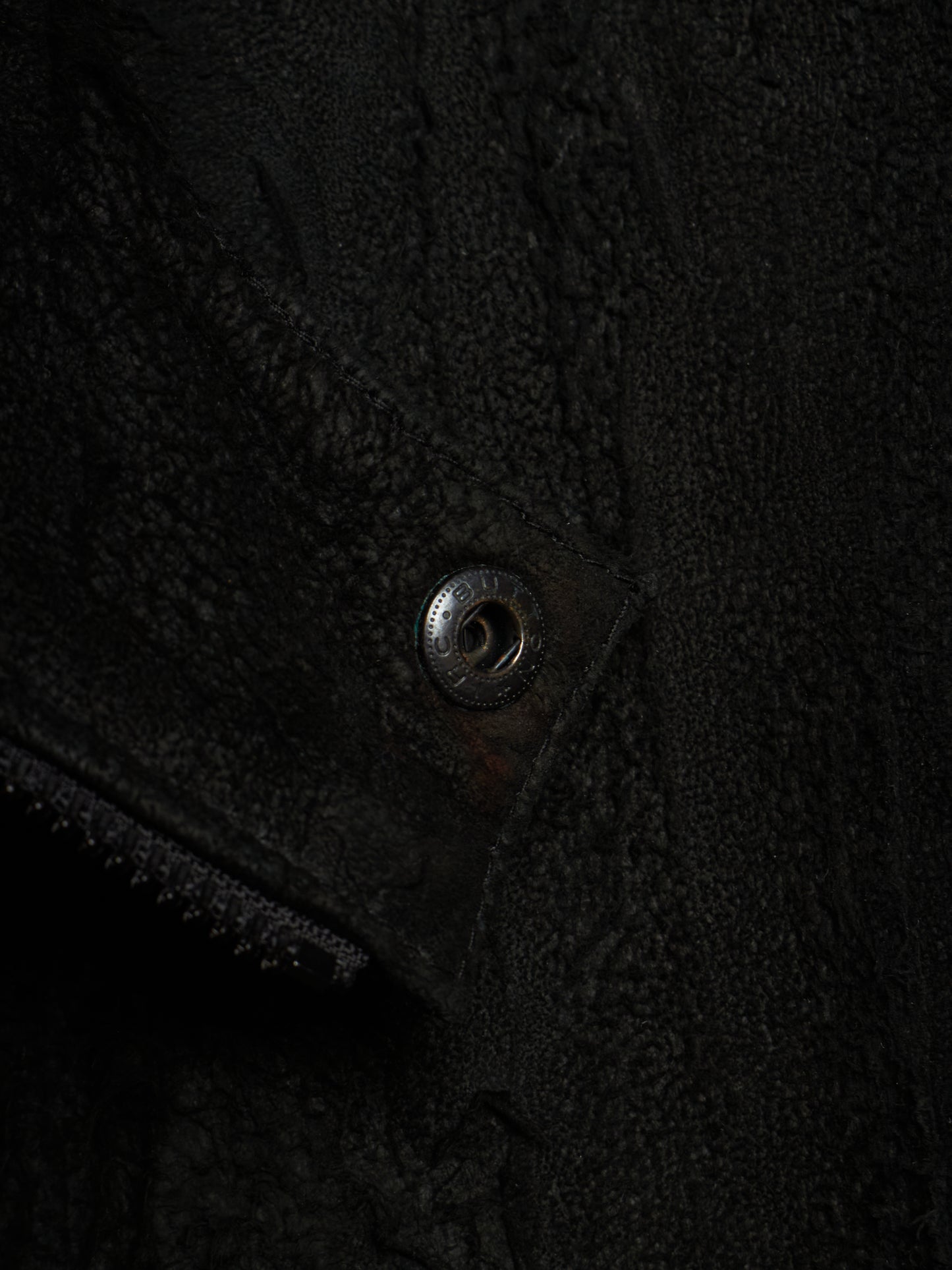 Close-up detail of a black textured fleece or sherpa garment with a metal snap button closure.