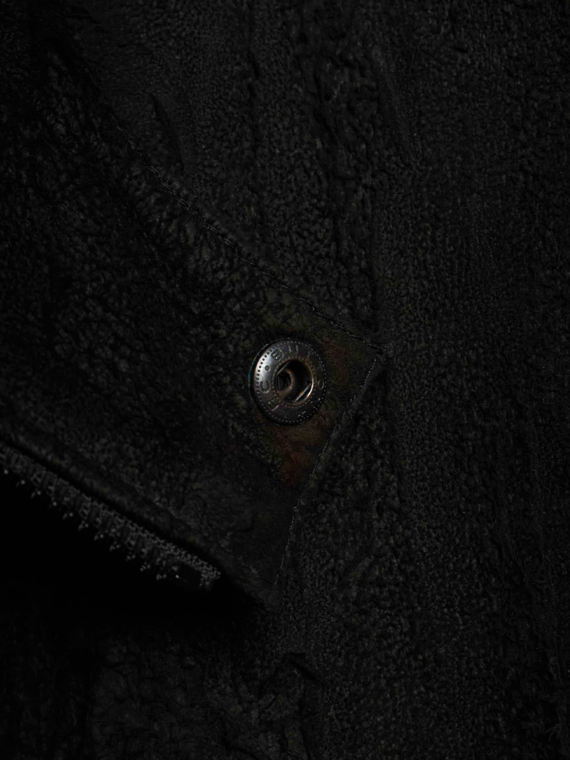 Close-up detail of a black textured fleece or sherpa garment with a metal snap button closure.