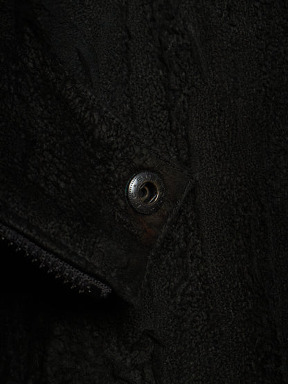 Close-up detail of a black textured fleece or sherpa garment with a metal snap button closure.