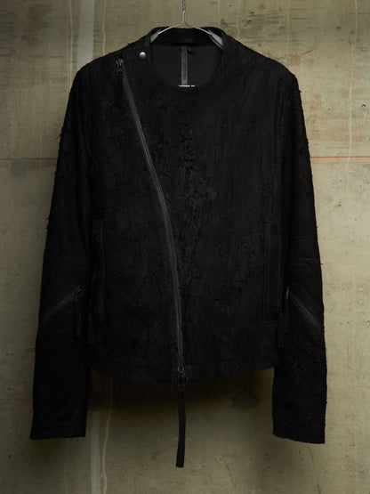 A black textured jacket with an asymmetrical zipper, hanging on a black hanger against a concrete wall.