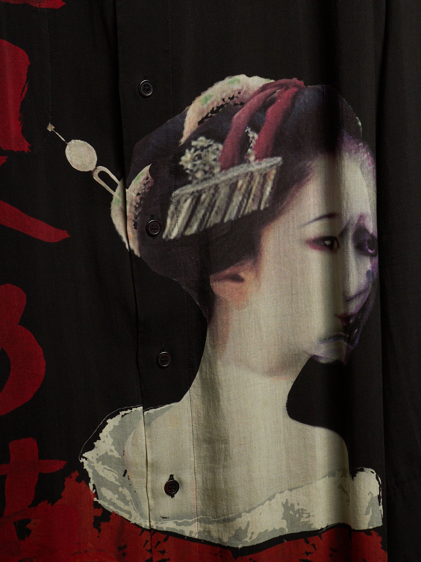 A close-up of a black button-front garment featuring a large printed portrait of a woman in traditional Japanese styling, with red brushstroke accents and a cream-toned collar area.