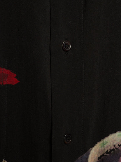 Close-up of a black button-front garment with a vertical placket, dark buttons, and partial abstract red and multicolor fabric details at the edges.