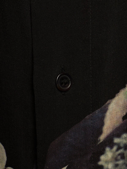 Close-up detail of a black button-up shirt featuring a single dark button and a subtle abstract floral pattern visible in the lower right corner.