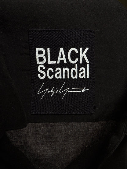 Close-up of a black fabric patch with white embroidered text reading 'BLACK Scandal' and a white signature-style logo, attached to a black garment.