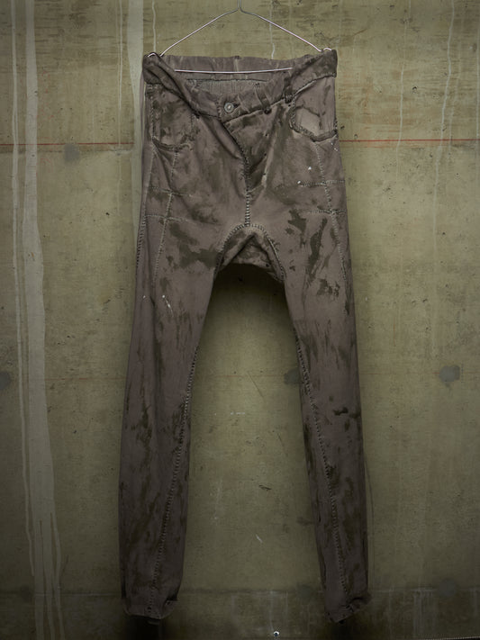 A pair of faded, distressed gray denim jeans hanging on a wire hanger against a textured concrete wall.