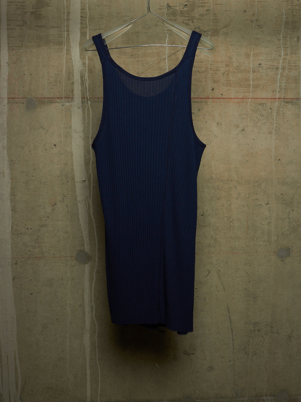A dark navy blue ribbed knit tank dress hanging on a clear plastic hanger against a textured concrete wall.