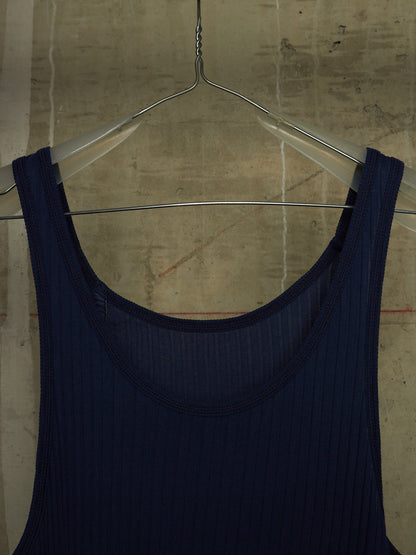 A dark navy blue ribbed tank top hanging on a clear plastic hanger against a textured concrete wall.