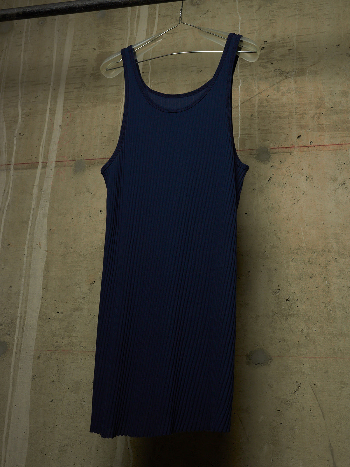 A dark navy blue ribbed knit tank dress hanging on a clear plastic hanger against a textured concrete wall.