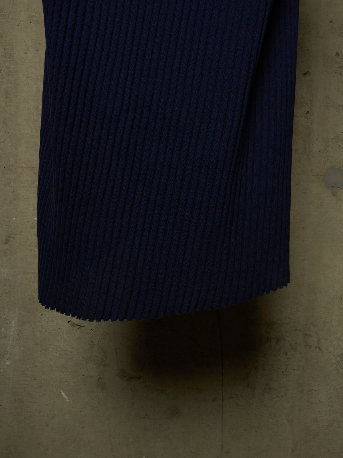 A close-up of dark navy pleated fabric, likely a pleated skirt or garment, laid flat on a concrete floor.