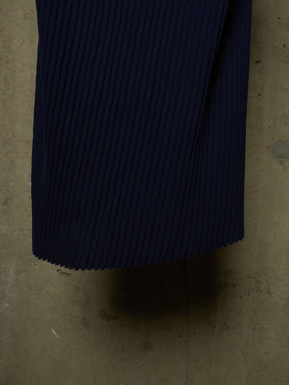 A close-up of dark navy pleated fabric, likely a pleated skirt or garment, laid flat on a concrete floor.