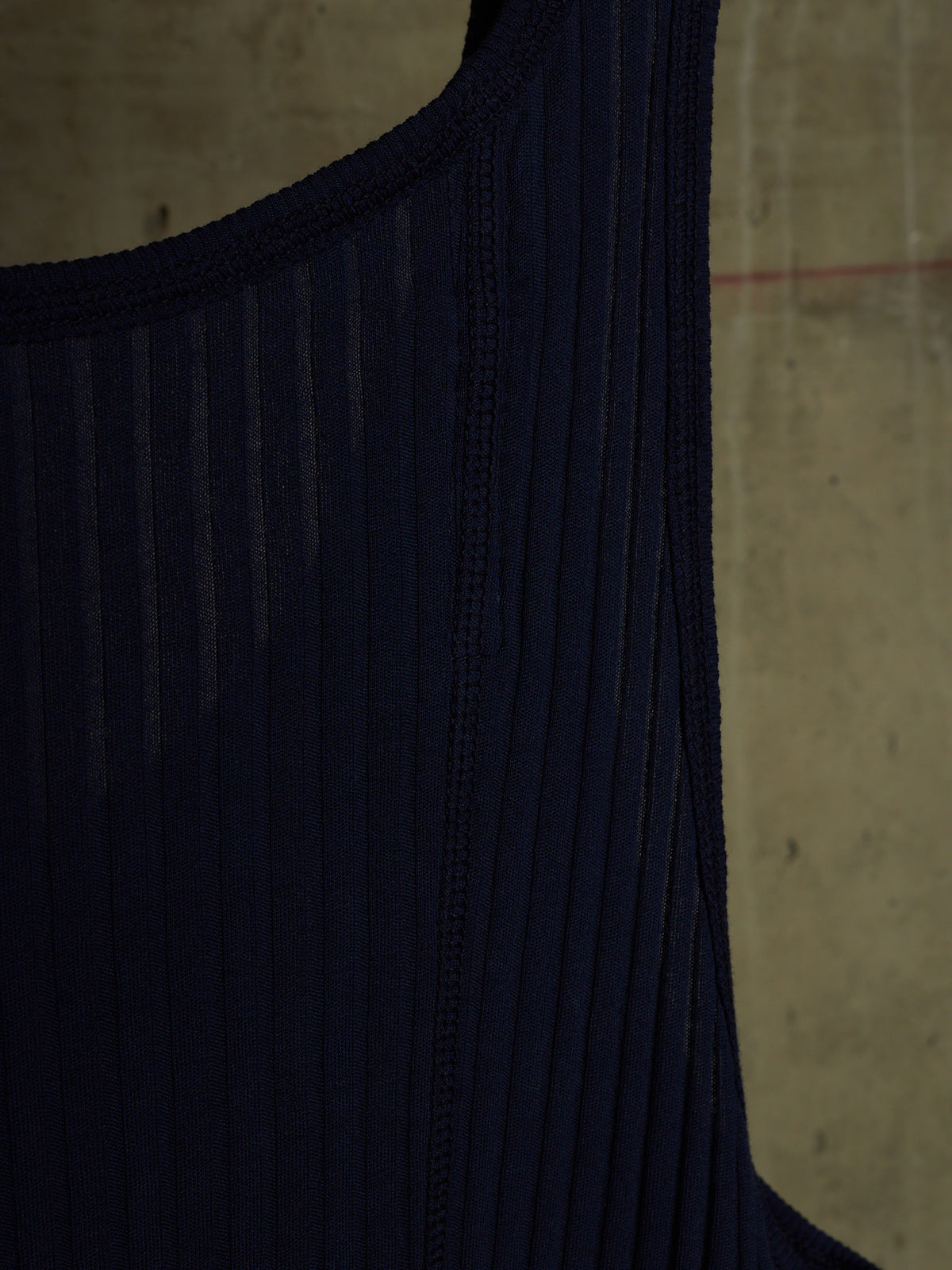 Close-up of a dark navy ribbed knit garment, showing the texture and neckline against a concrete wall background.