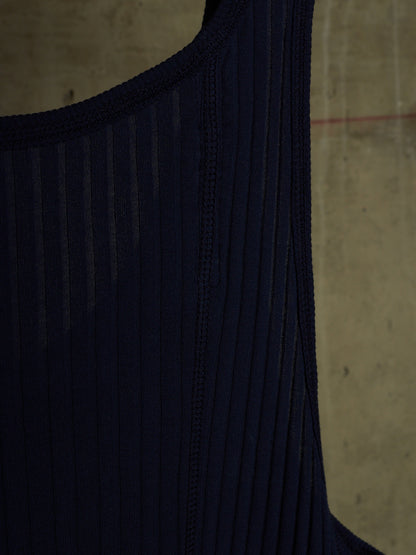 Close-up of a dark navy ribbed knit garment, showing the texture and neckline against a concrete wall background.