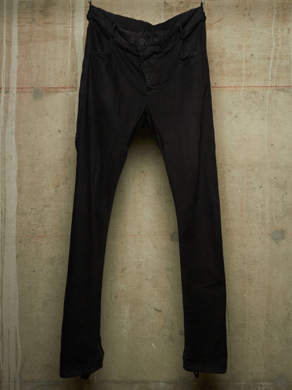 A pair of black slim-fit pants hanging against a textured concrete wall.