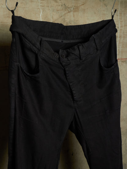 Black cotton trousers hanging from metal hooks against a textured concrete wall.