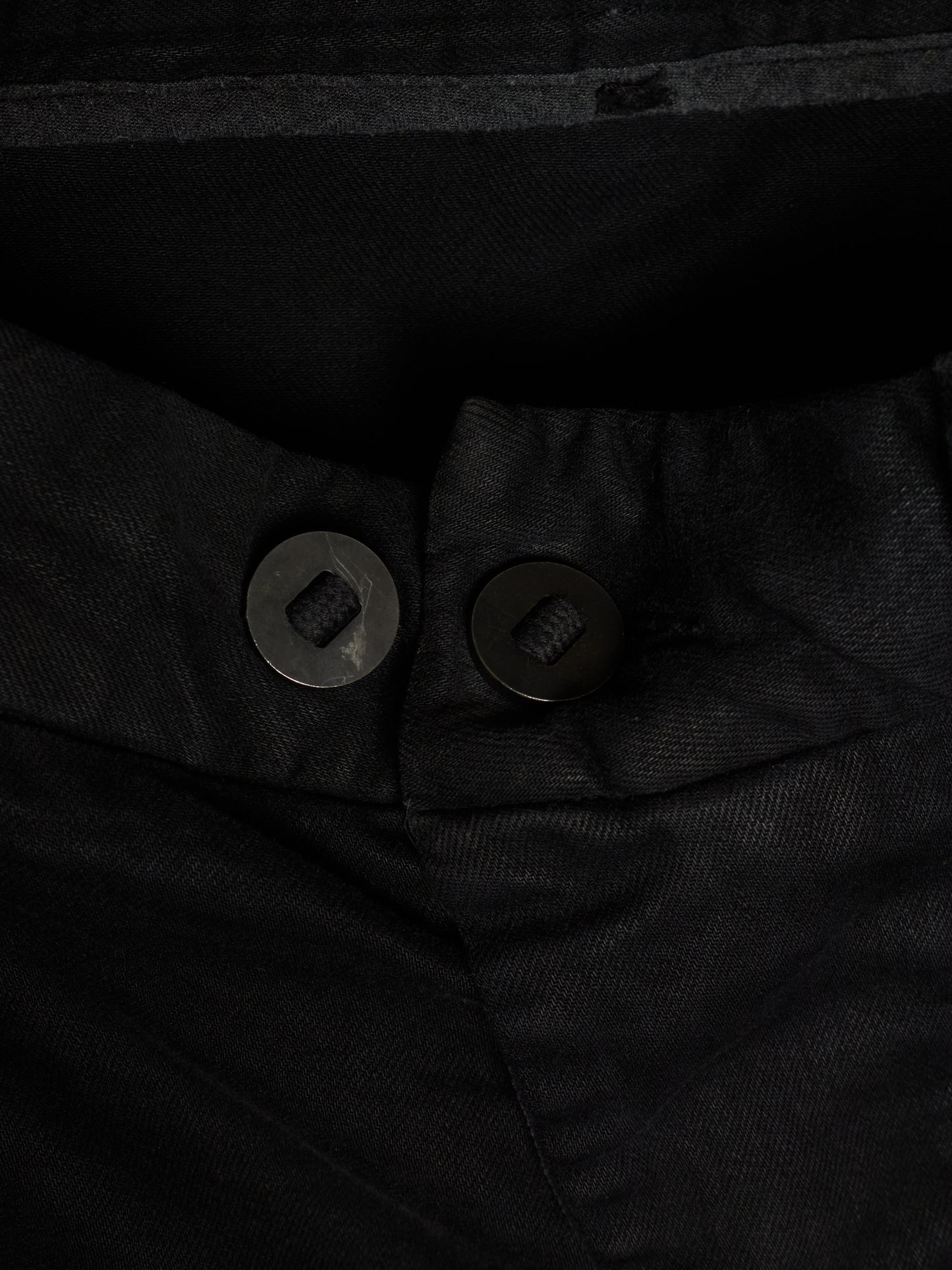 Close-up of black trousers showing the waistband, button closure, and textured fabric.