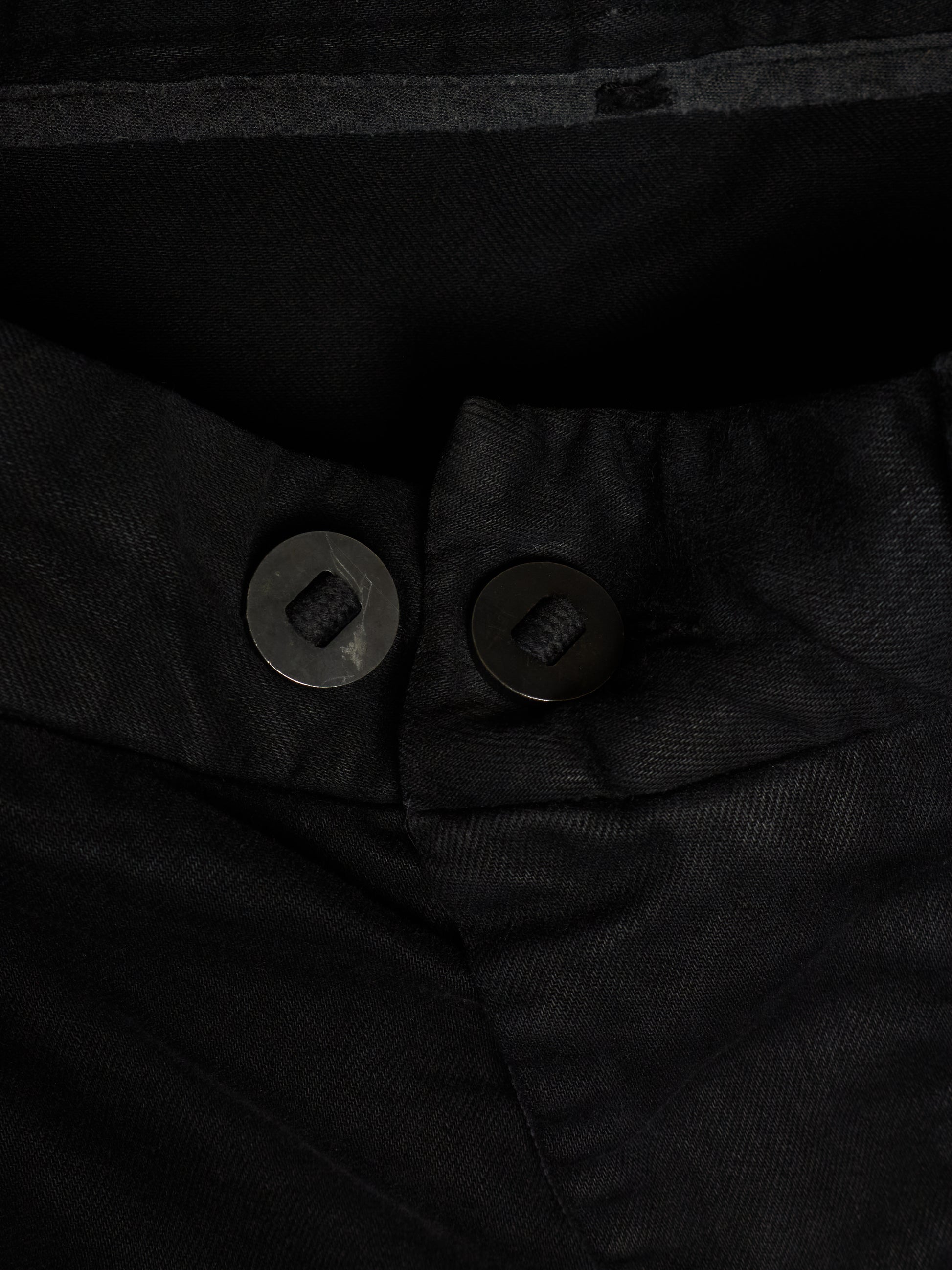 Close-up of black trousers showing the waistband, button closure, and textured fabric.