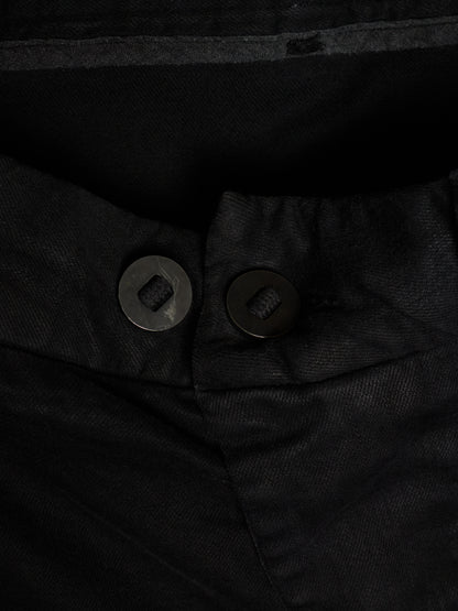 Close-up of black trousers showing the waistband, button closure, and textured fabric.