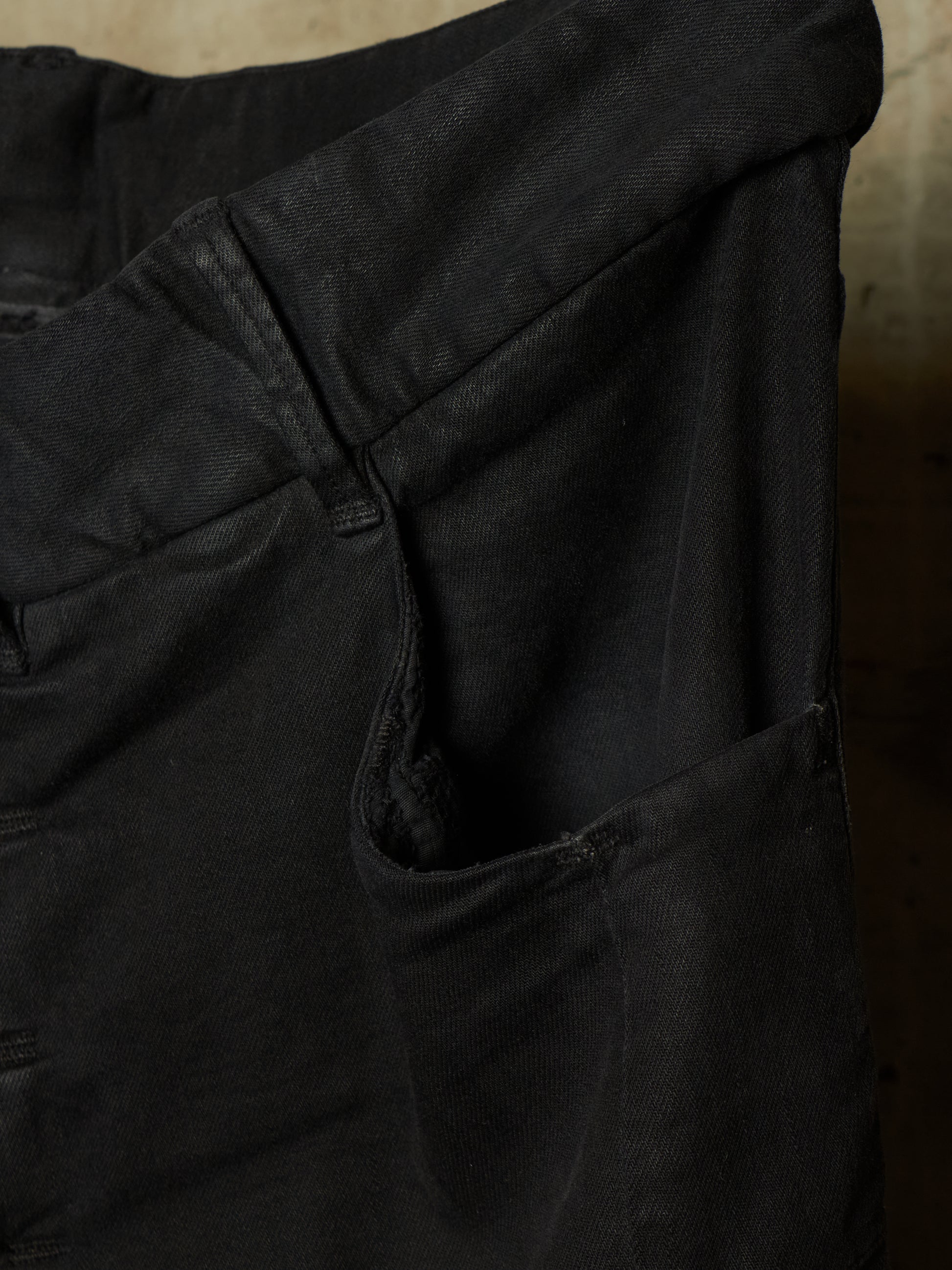Close-up detail of black denim pants showing the waistband, belt loop, and side pocket stitching.
