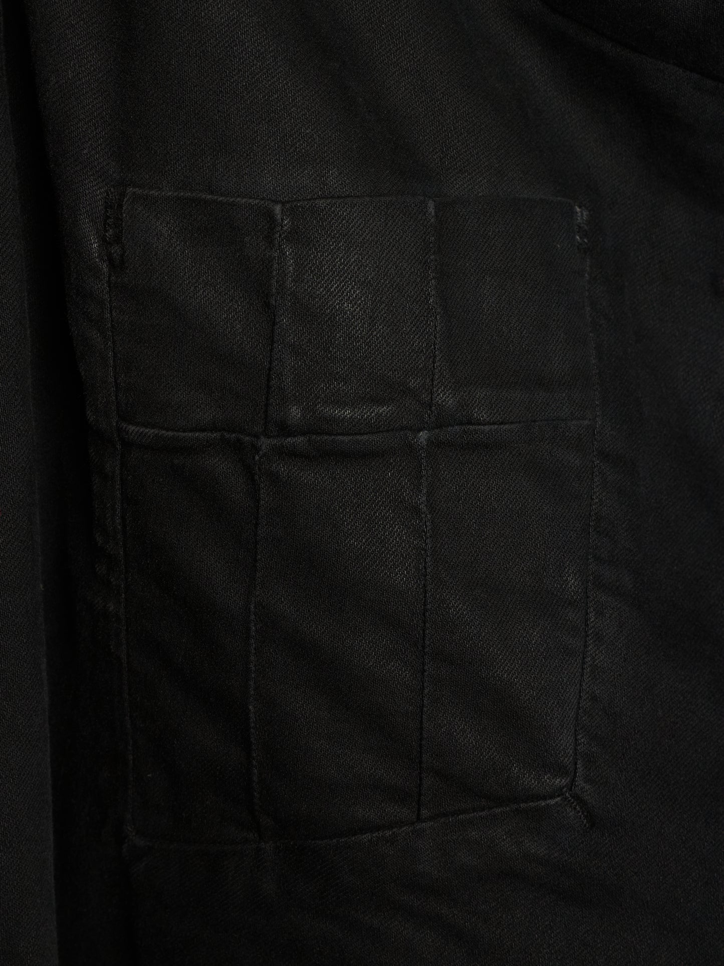 Close-up of a black fabric garment showing a large rectangular patch pocket with stitched seams.