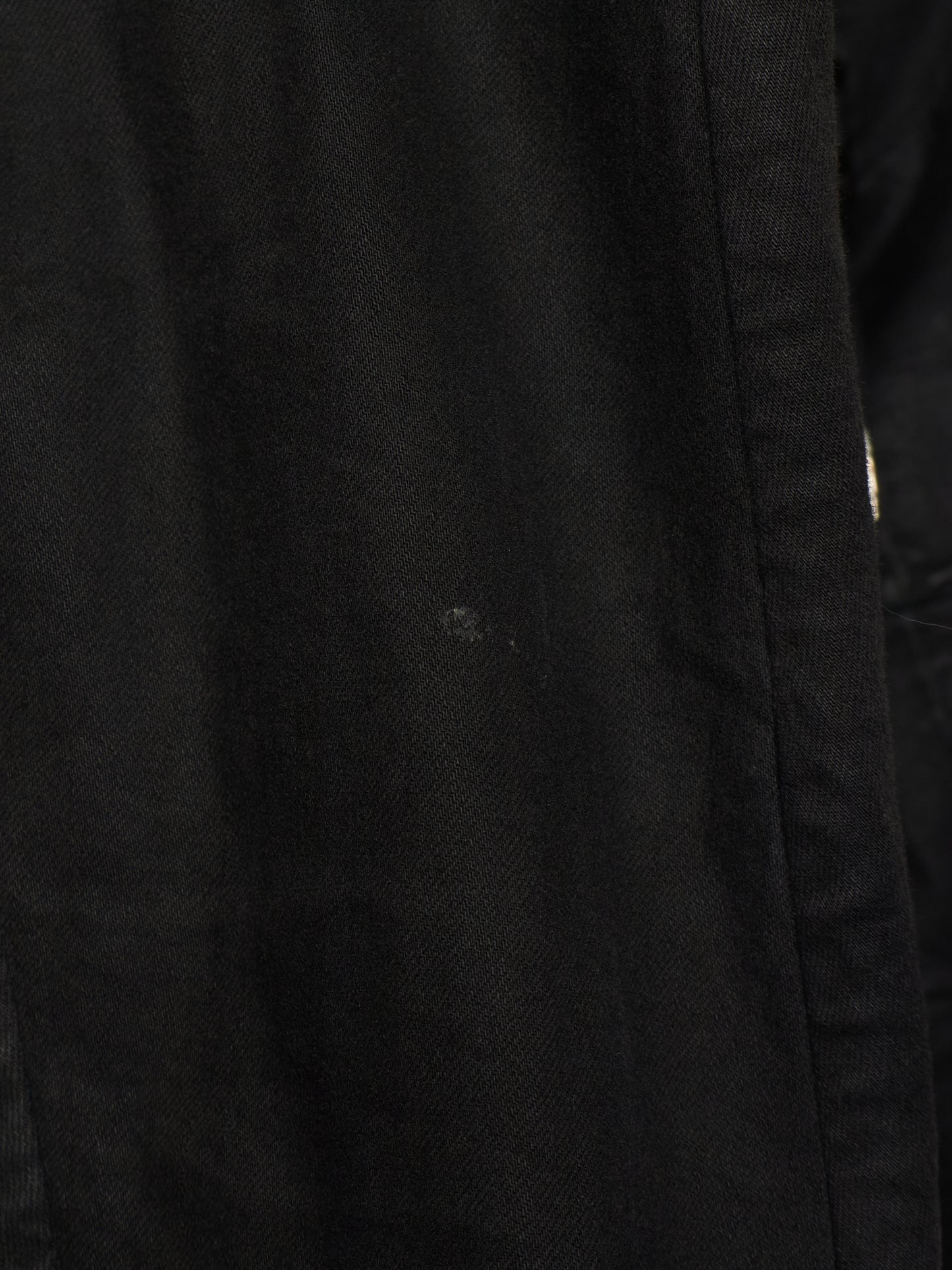 Close-up of a black textured fabric surface with a visible seam and a small light speck on the material.