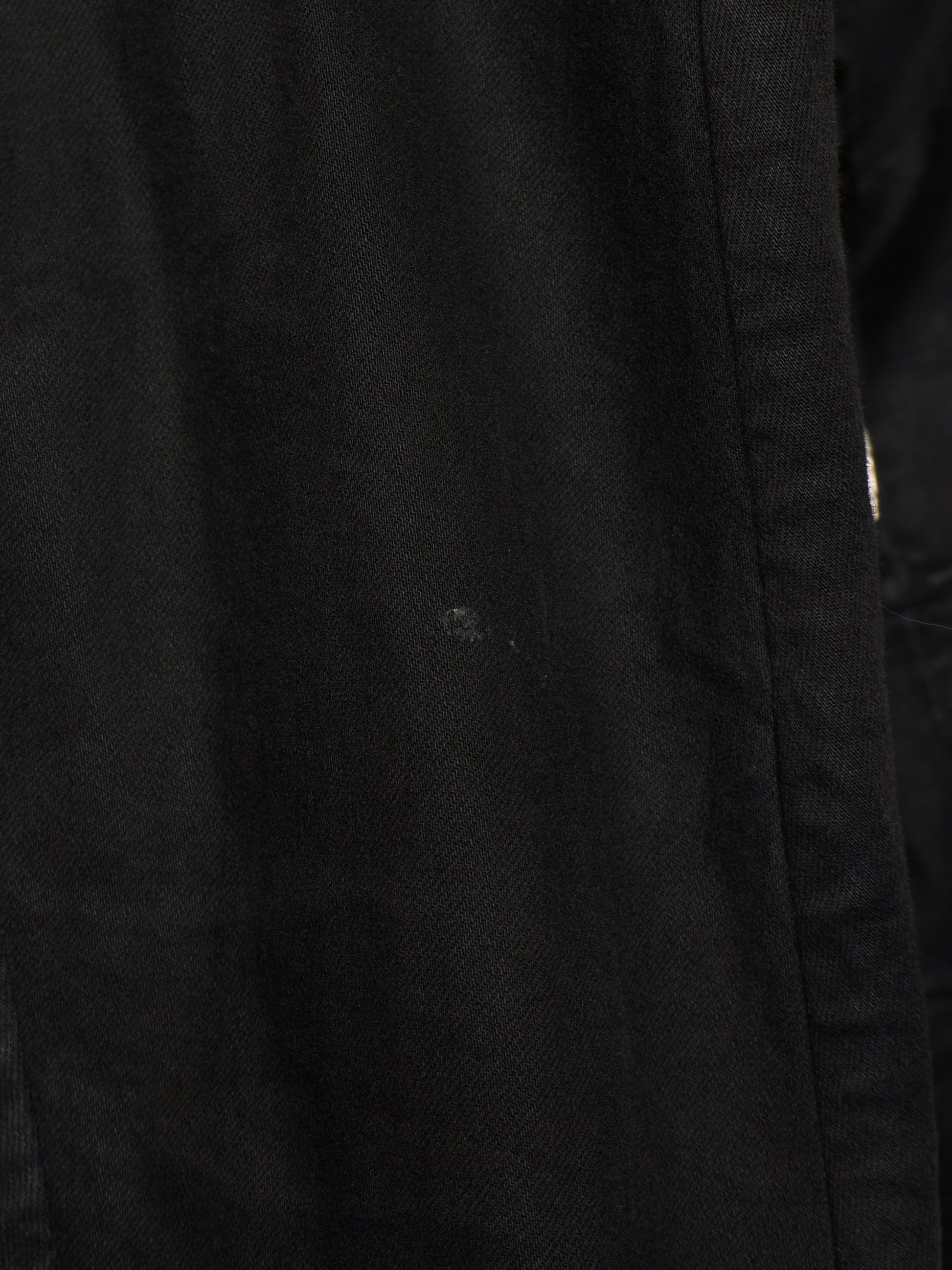 Close-up of a black textured fabric surface with a visible seam and a small light speck on the material.