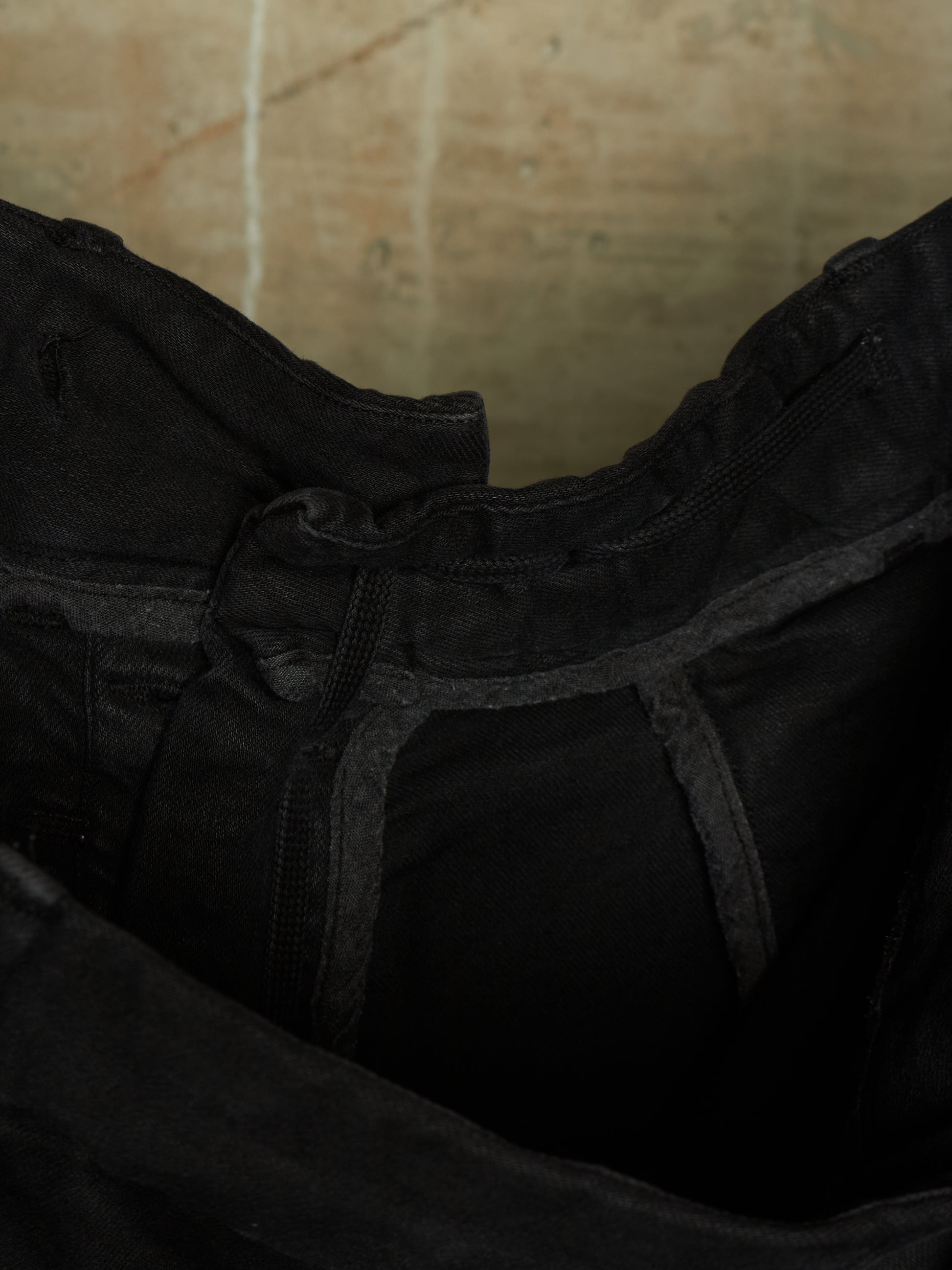 Close-up detail of a black garment, showing the inner waistband, zipper, and dark fabric texture against a warm beige background.