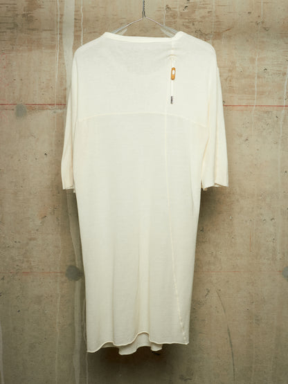 An off-white, semi-sheer long-sleeve dress with a wide collar, hanging on a clear plastic hanger against a textured concrete wall.