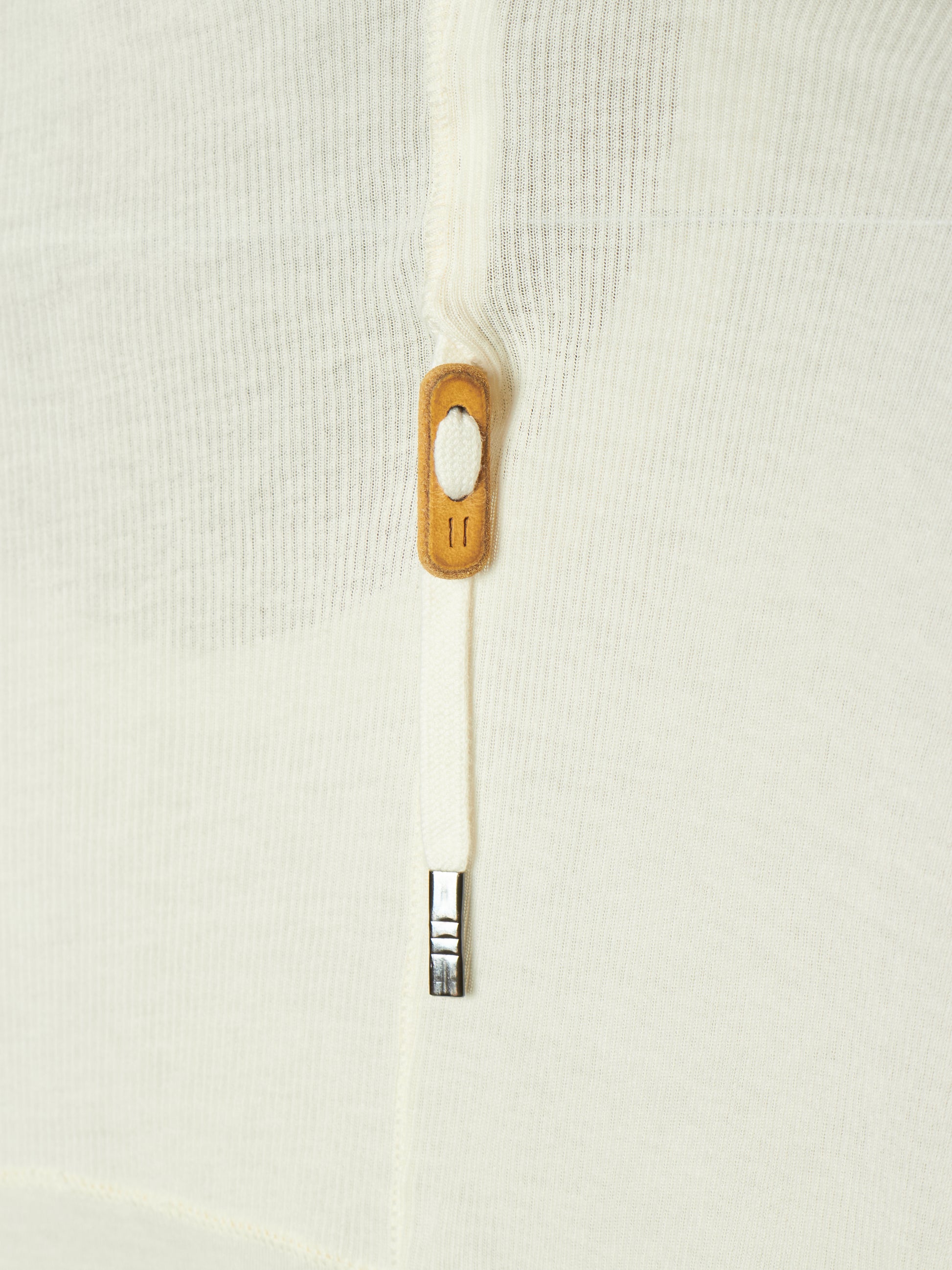 Close-up of a white textured knit garment featuring a white zipper with a light brown wooden pull tab and a silver metal tip.