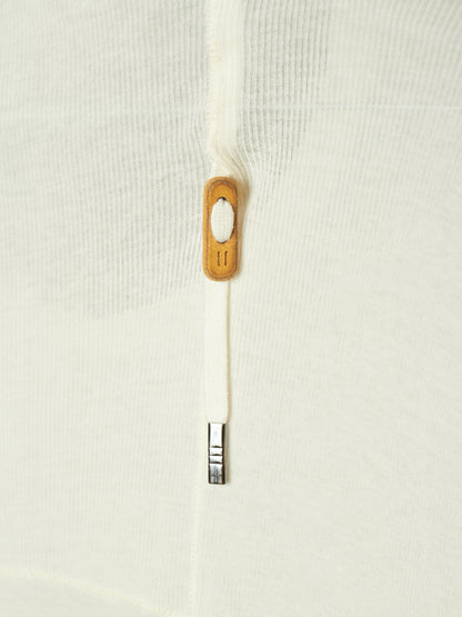 Close-up of a white textured knit garment featuring a white zipper with a light brown wooden pull tab and a silver metal tip.