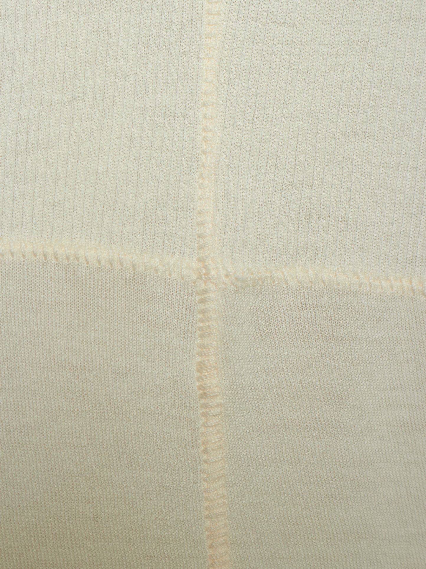 Close-up of a cream-colored knit fabric with a visible cross-stitch pattern and fine ribbed texture.