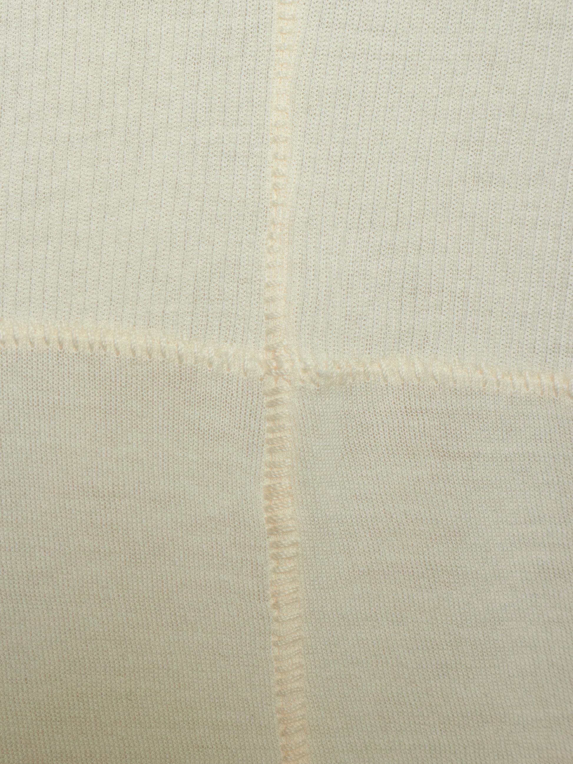Close-up of a cream-colored knit fabric with a visible cross-stitch pattern and fine ribbed texture.