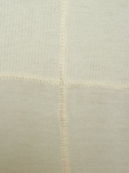 Close-up of a cream-colored knit fabric with a visible cross-stitch pattern and fine ribbed texture.