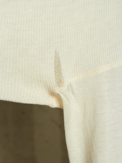 Close-up of a cream-colored ribbed knit garment, showing the texture of the fabric and a small frayed edge near the hem.