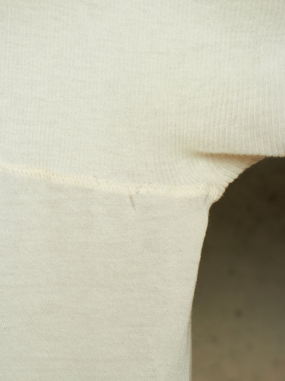 Close-up detail of a cream-colored knit garment, showing the ribbed texture and a folded seam against a neutral background.