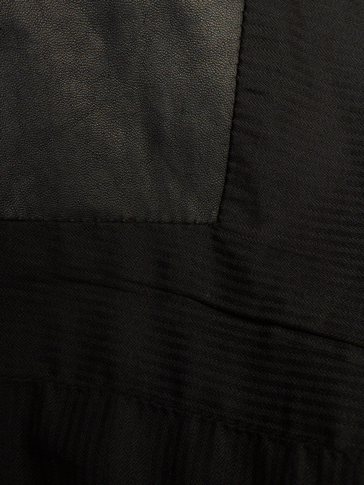 Close-up of a black garment showing different fabric textures, including a smooth matte panel and a ribbed knit section.
