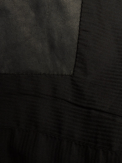 Close-up of a black garment showing different fabric textures, including a smooth matte panel and a ribbed knit section.