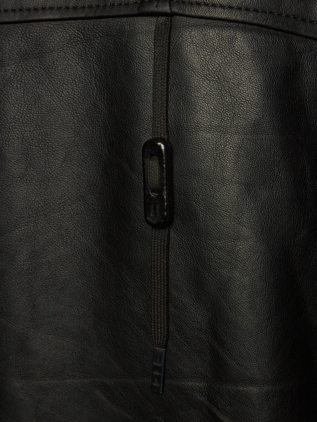 Close-up of a black leather jacket showing a vertical zipper with a black metal pull tab and the textured leather surface.