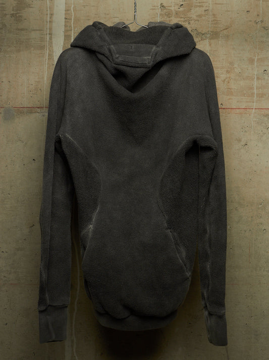 A dark charcoal gray oversized hoodie with a draped, asymmetrical neckline, hanging against a textured concrete wall.