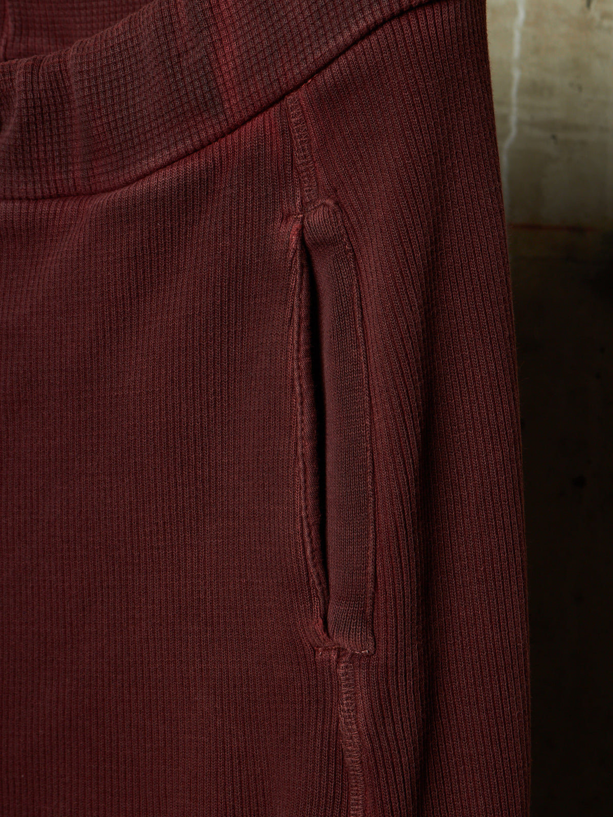 Close-up of a ribbed burgundy fabric garment showing a vertical seam and a side pocket opening.