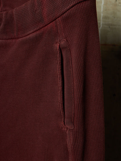 Close-up of a ribbed burgundy fabric garment showing a vertical seam and a side pocket opening.