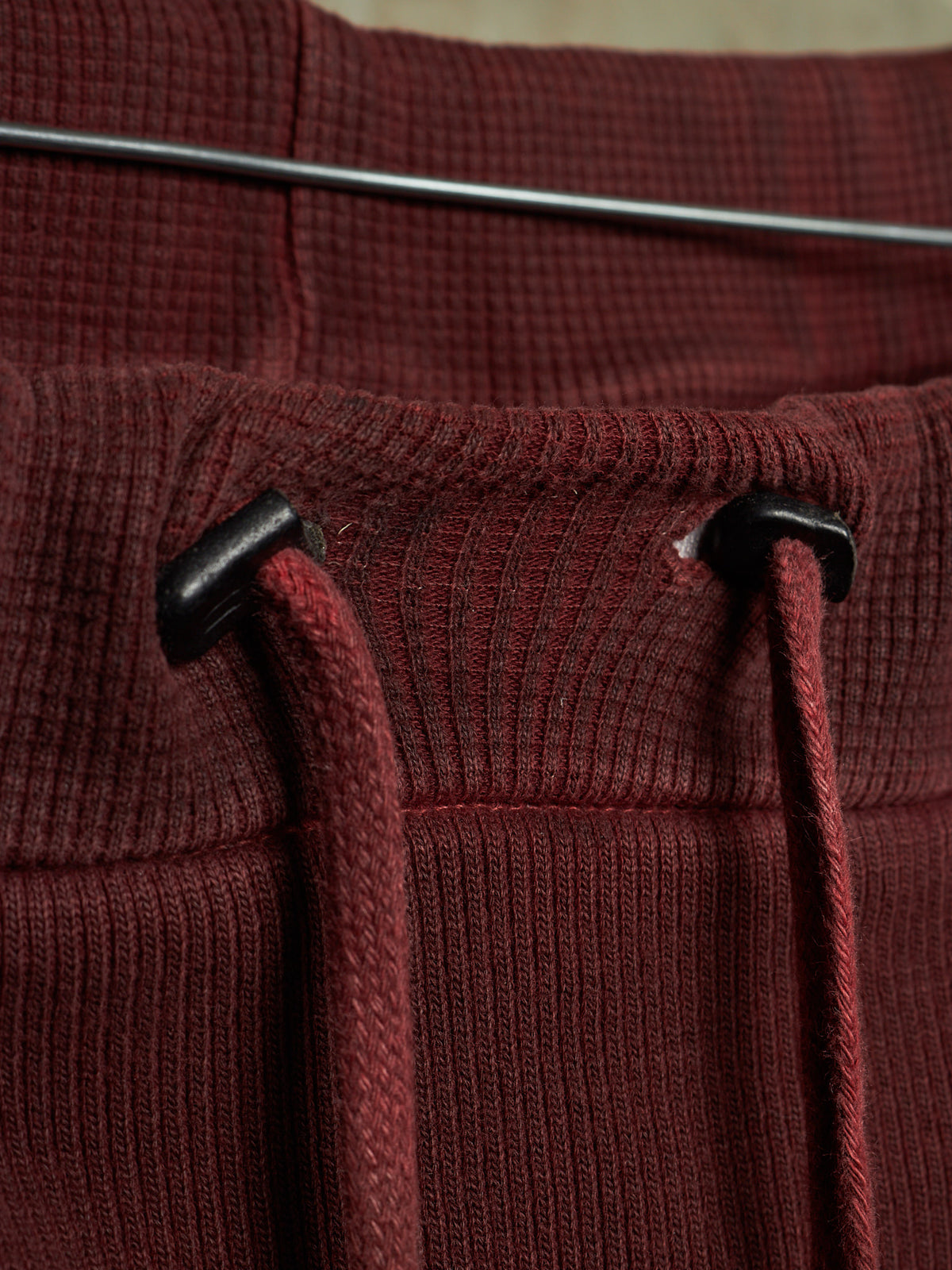 Close-up of a ribbed knit garment in deep burgundy with matching drawstrings and black plastic toggle hardware.