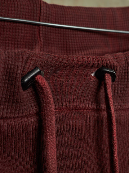 Close-up of a ribbed knit garment in deep burgundy with matching drawstrings and black plastic toggle hardware.