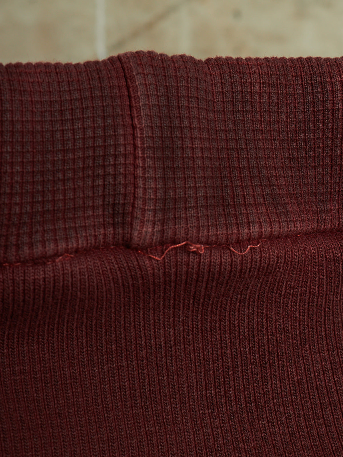 Close-up of a dark burgundy ribbed knit fabric, showing the texture and a small loose thread detail near the center seam.