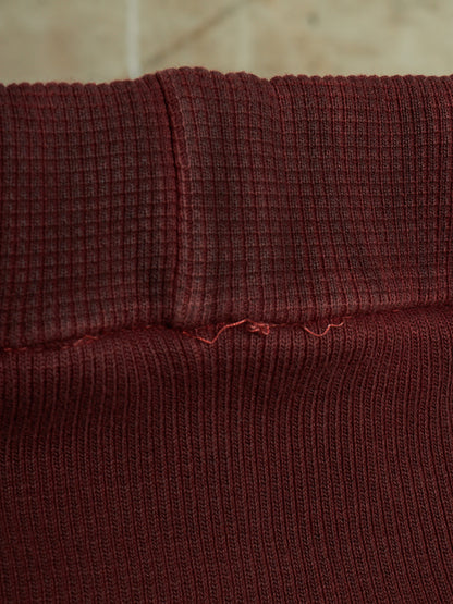 Close-up of a dark burgundy ribbed knit fabric, showing the texture and a small loose thread detail near the center seam.
